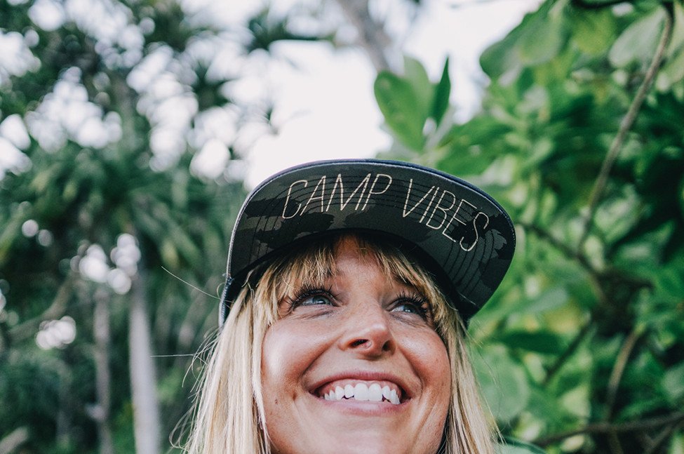 Camp Vibes - Woman smiling with a camo hat that says Camp Vibes
